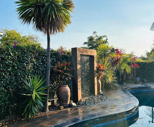 Tropical backyard pool with modern corten steel water feature