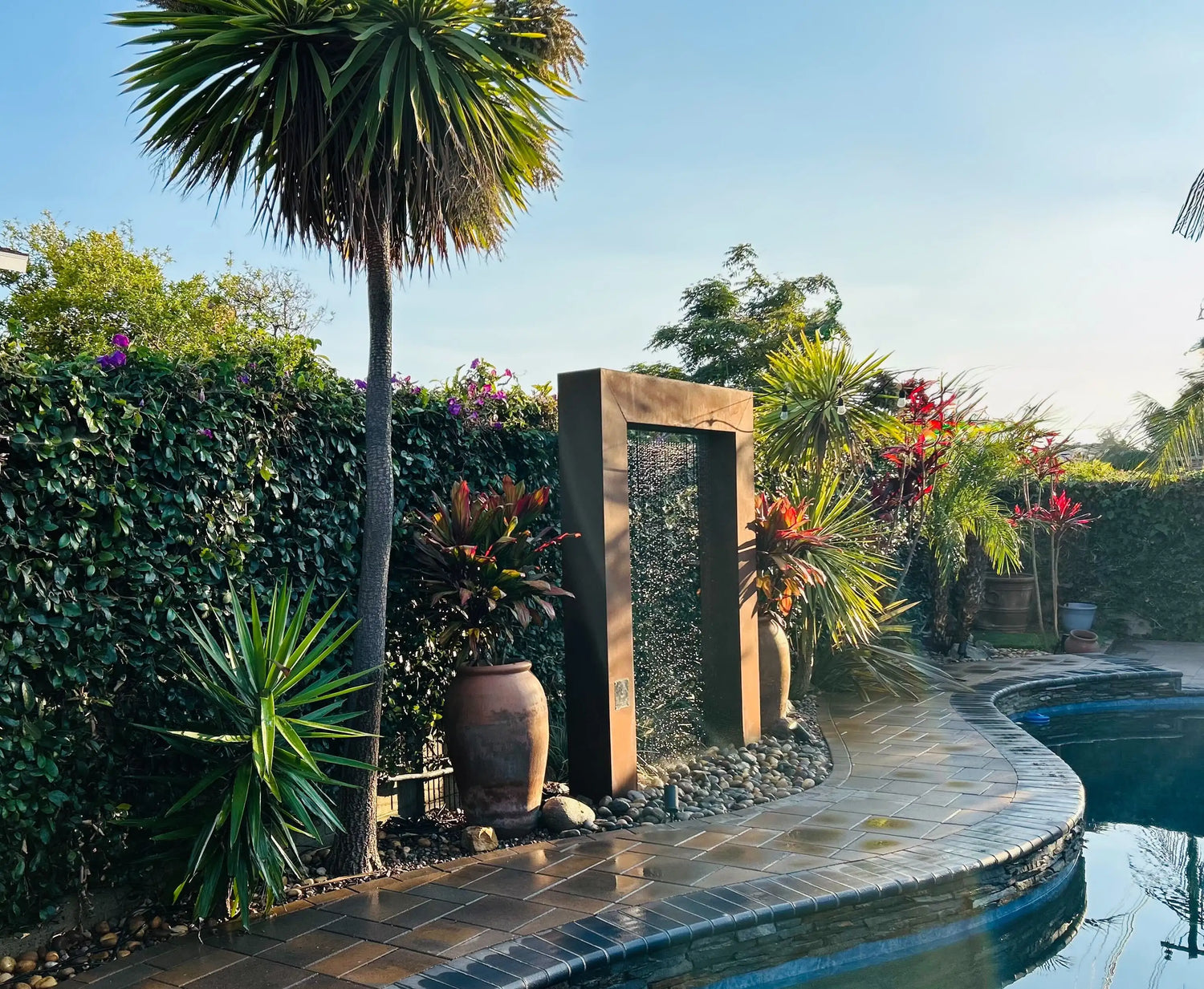Tropical backyard pool with modern corten steel water feature