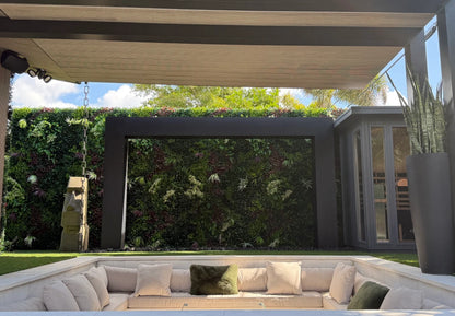Black steel rain curtain fountain door built into a shaded pergola with a lush living plant wall backdrop above a sunken outdoor lounge seating area.