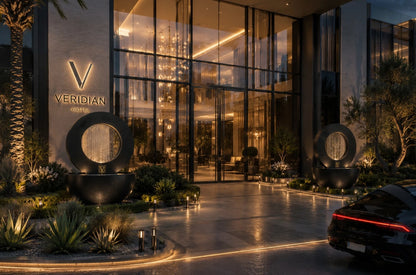 Two black outdoor planter fountains with integrated rain curtains framing a modern glass hotel entrance and illuminated driveway at night.