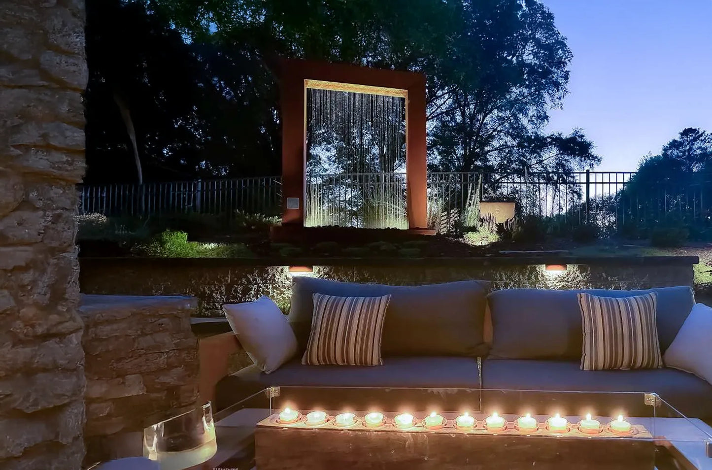 Corten steel rain curtain fountain door with integrated LED lighting, creating a striking modern water feature for a luxury backyard patio, contemporary landscape design, and elegant outdoor living space at night.