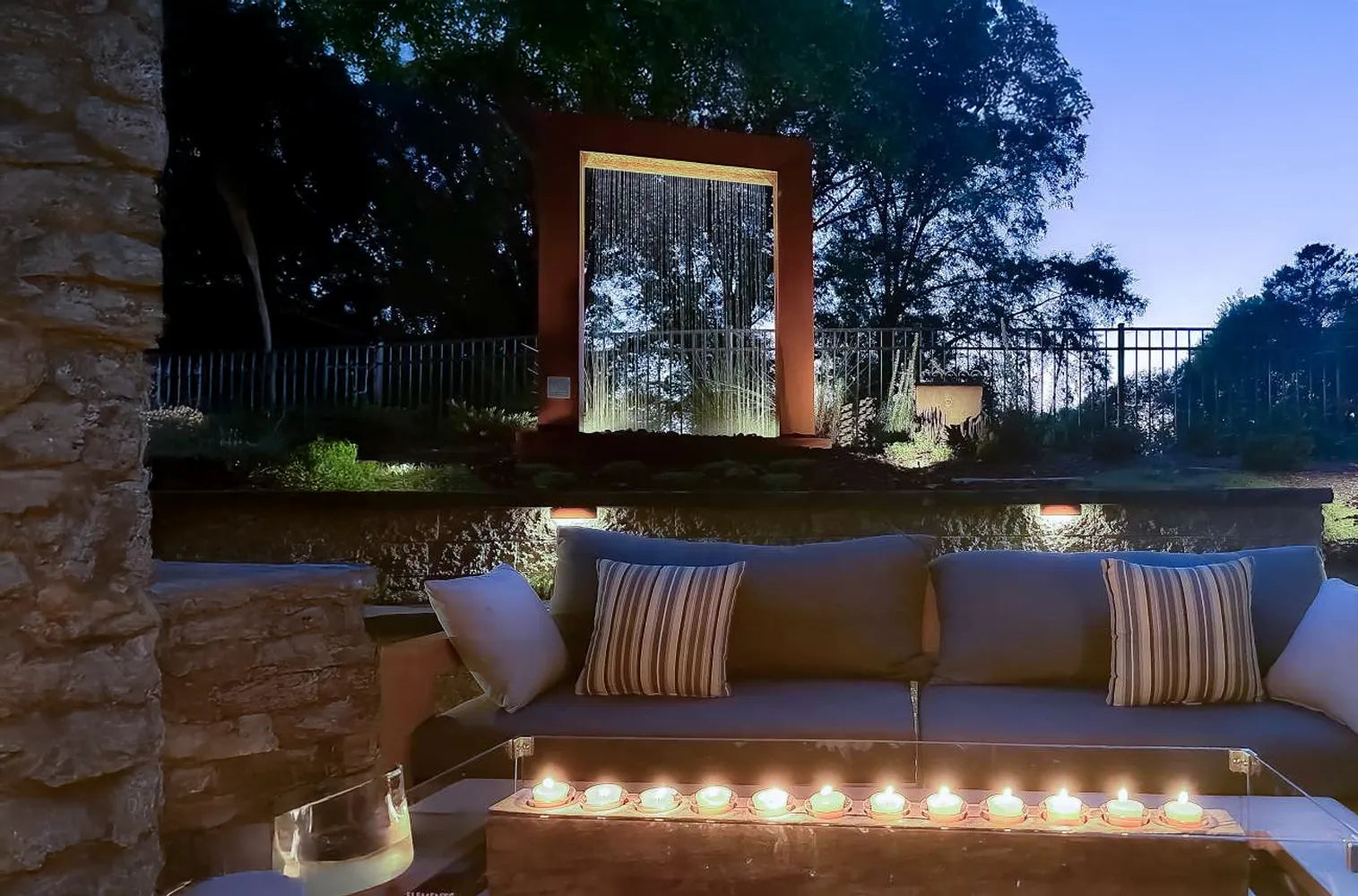 Corten steel rain curtain fountain door with integrated LED lighting, creating a striking modern water feature for a luxury backyard patio, contemporary landscape design, and elegant outdoor living space at night.