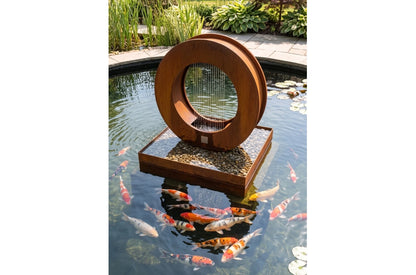 Corten steel ring fountain on a square pebble base set in a koi pond with lily pads and lush garden planting